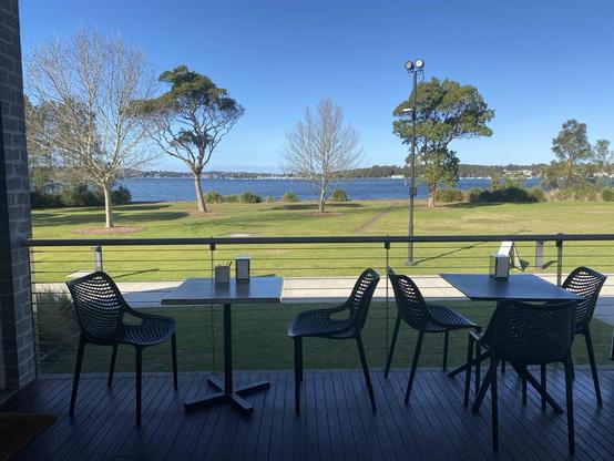 Cafe tables on the shaded terrace overlooking the green parkland and blue lake.