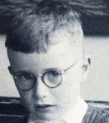 Black and white photo of a young boy wearing round glasses and a formal shirt.