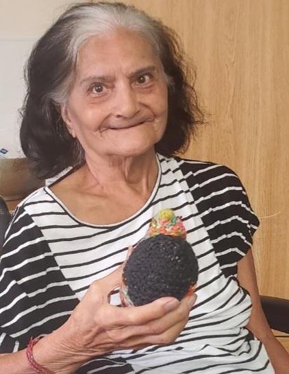 An older Pakistani woman, with black hair in a short bob, a white streak across the front, in a black and white short sleeved top, holding a multicolor little chickie, and she is smiling, which is everything