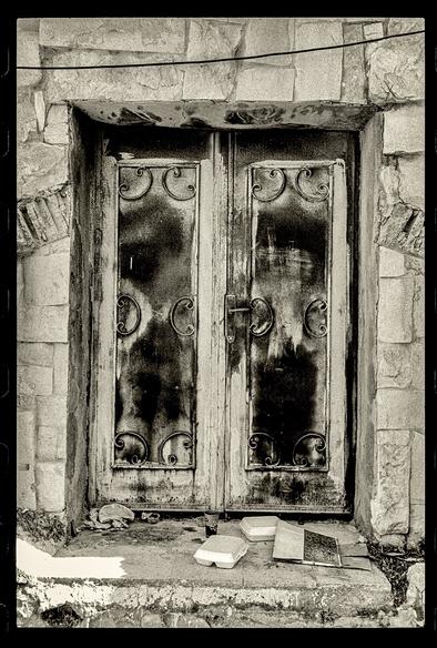 A black and white photo of a beat up old metal door on a back alley in the tla’a al-Ali neighborhood of Amman.