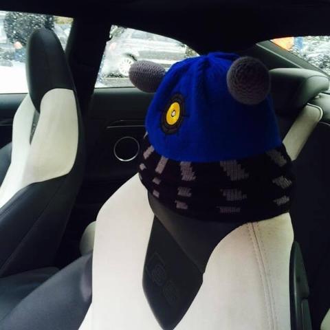 Knit cap styled after a blue Dalek placed on the driver side's headrest inside of a car.
