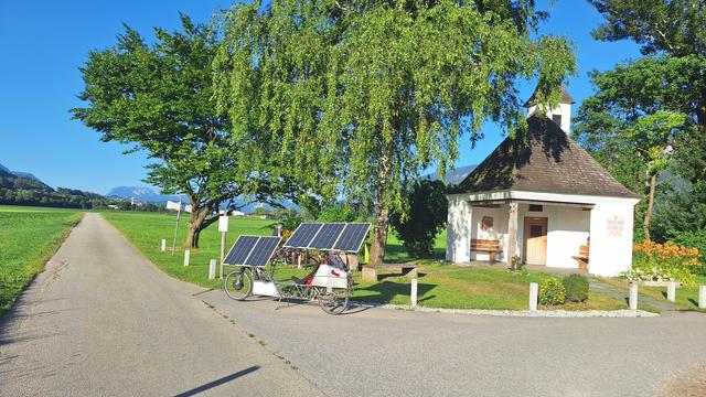 Solar bike charging by the side of the road near chapell under the trees.