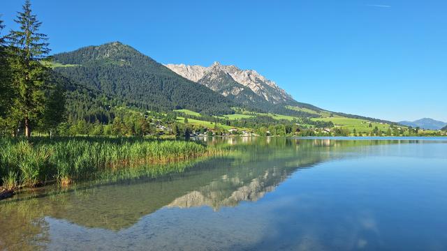 Walchsee: blue lake, green hill covered by forest, white rocky peak, blue sky