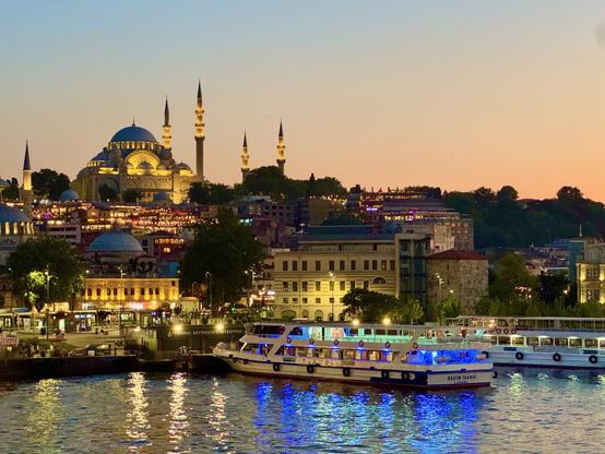 a large lit up mosque on top of a hill, the golden horn below