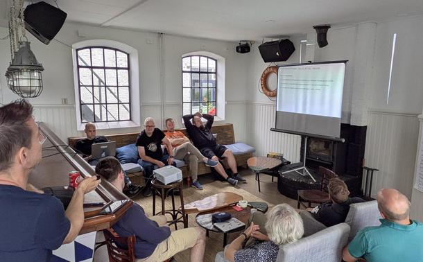 People sitting in a bar room and looking at presentation slides. Active discussions on the presented features.