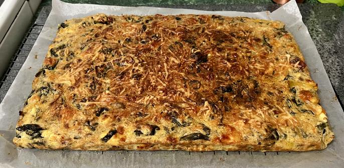 a large rectangular slab of cooked cheese and spinach and egg and vegetables sitting on top of a sheet of baking paper