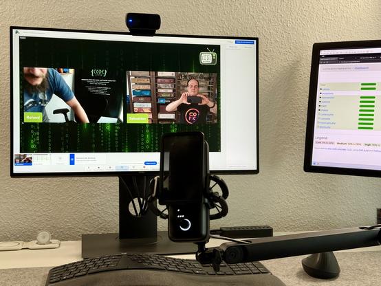 Photo of my desk with keyboard, two screens, a camera, and a microphone