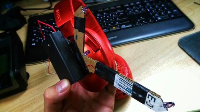 A cardboard contraption with 3IR LED and a battery compartment strapped to headphones
