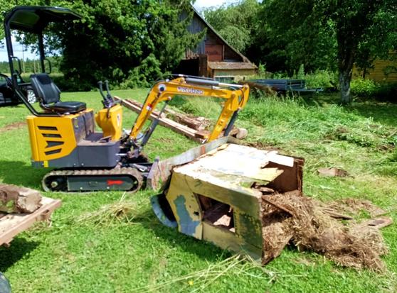 Mini excavator has smashed up an old dog house and knocked it over. Dirty old straw is spilling out of the bottom. The photo is completely out of focus.