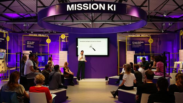 Julia Gundlach bei ihrem Vortrag beim Civic Coding x Mission KI Forum. Sie steht im Plenum links neben einem Bildschirm, der Informationen zu ihrem Beitrag zeigt. Im Publikum sitzen verschiedene Personen, die interessiert zuhören.
