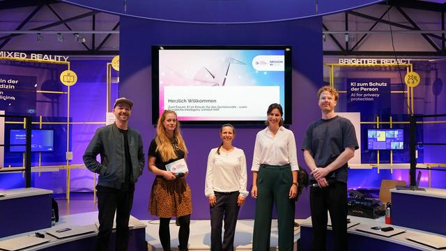 Es stehen die Moderator*innen und Expert*innen von dem Civic Coding x Mission KI Forum auf der Bühne vor dem Begrüßungsbildschirm. 
Von links nach rechts stehen Matthias Hild, Nora Zupan, Marije Weber, Julia Gundlach und Mathes Hünsche.