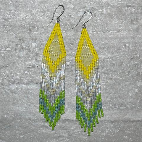 A pair of yellow, silver, green, and turquoise beaded fringe earrings on a stone background
