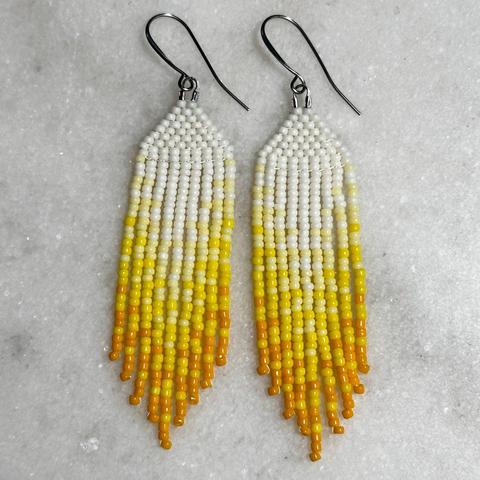 A pair of white to yellow ombre beaded fringe earrings on a marble background
