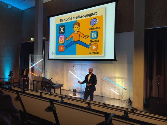 Rudy van Belkom in een collegezaal. Op de achtergrond een dia met aan de linkerkant onvrije platforms en rechts federatieve alternatieven.