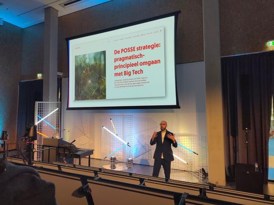 Rudy van Belkom in een collegezaal. Op de achtergrond een dia over de posse strategie rondom big tech van public spaces.