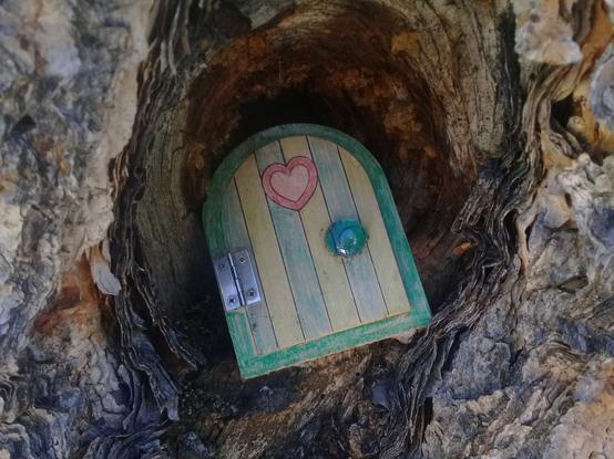 tucked deep in the natural recesses of a tree, a tiny (maybe 2 inch) hand-painted door on a hinge, with hellow/green stripes, a heart, and a flat marble glued on - perhaps an entry point to a fairy realm?