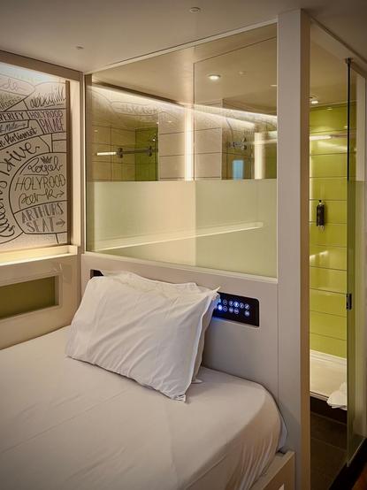 Compact hotel room: headboard of bed is window to shower room
