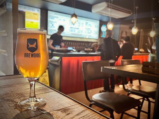 Glass of beer on table, bar and beer menu in background
