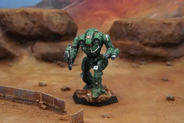 A painted miniature of an Axman 'Mech.  It is green with white stripe highlights.  The cockpit glass is red.  The sunburst emblem of the Federated Suns is on the head.  The number "24" is on the right torso.  The miniature is photographed on desert terrain.