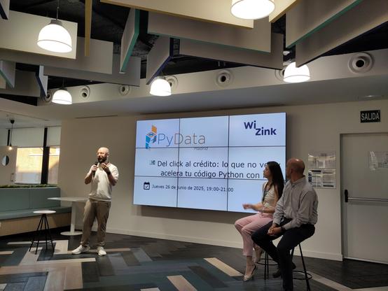 Foto de unas personas en un escenario junto a una pantalla gigante en la que se ven los logos de PyData Madrid