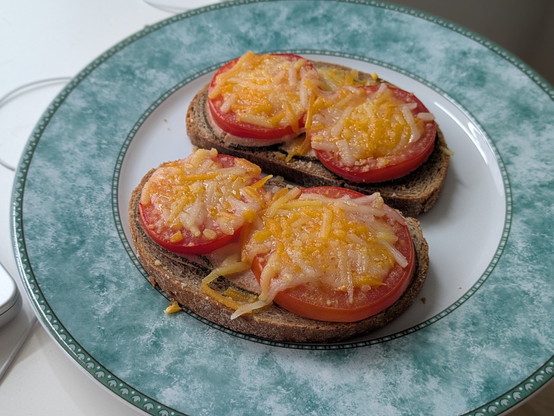 Auf dem Bild sieht man zwei Scheiben dunkles Brot (vermutlich Roggenbrot oder Mischbrot), die mit dicken Tomatenscheiben und Wurstscheiben belegt sind. Darüber ist eine Schicht geriebener veganer Käse, der gerade frisch geschmolzen ist.

Das Ganze sieht nach einer einfachen, aber schmackhaften Mahlzeit aus.