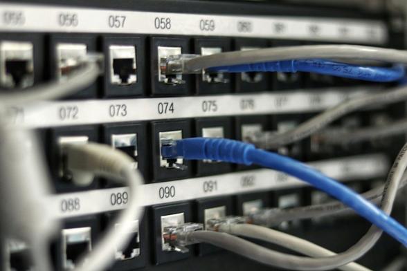 Patch panel with numbered ports that has grey and blue network cables connected to the ports.  Some ports are empty.