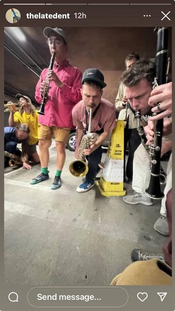 A wide, low angle shot of some musicians appearing very intent on blowing hard. There are several Bb clarinets, an alto clarinet, a baritone saxophone (that's me), a trumpet, and an alto saxophone. We're mostly bent low toward the pavement in a dirty parking garage. There's also a yellow "wet floor" warning cone, for some reason. This is actually not a posed shot - we are rehearsing the piece for Saturday. Posted to instagram by account handle "thelatedent".