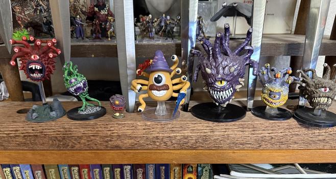 Seven Beholder miniatures in a row, with a Mr. Potato Head Beholder at center. The little Beholder to the left of it is an old Grenadier miniature from the early 80s that was one of the first Beholder figures sold.
