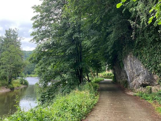 Ein Radweg am Fluss entlang, rechts Felsen, dazu viele Bäume