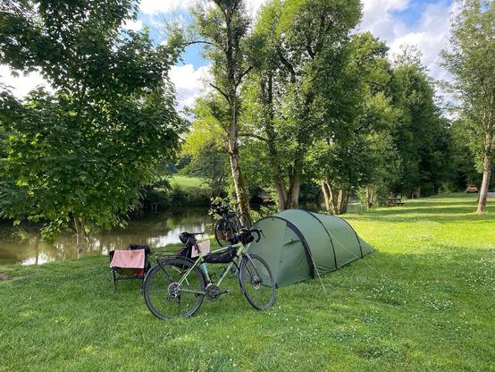 Das Zelt und die Räder stehen auf einer Wiese neben dem Fluss