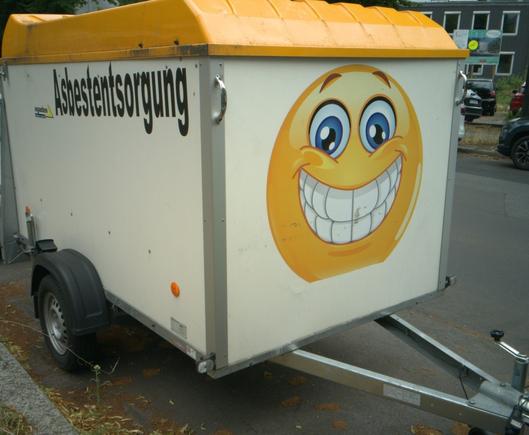 a trailer with the text "asbestentsorgung" (asbestos disposal) and a smiley with an extremely wide smile on the front side