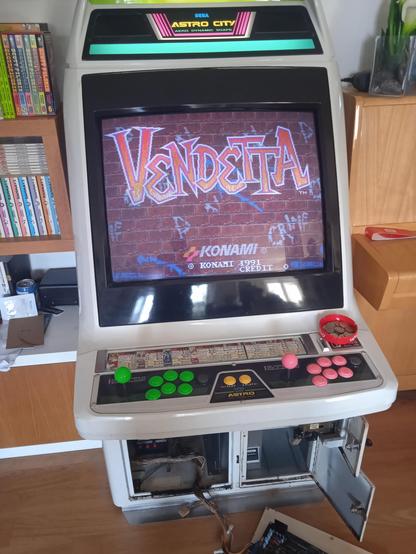 Un cabinato SEGA Astro City acceso. Gli sportelli in basso sono aperti e i cavi con l'attacco jamma raggiungono una PCB posata a terra. Sullo schermo si legge la scritta "Vendetta", su un muro di mattoni virtuale.