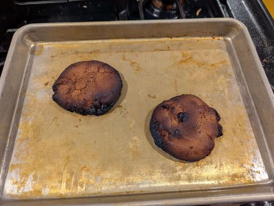 A sheet pan with 2 burned cookies on it.