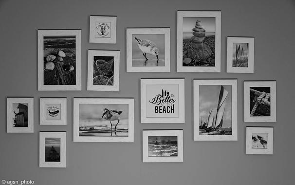 Ein Schwarz-Weiß-Bild einer Innenwand, dekoriert mit 15 kleinen gerahmten Fotos in verschiedenen Formaten. /
A black and white image of an interior wall decorated with 15 small framed photos in different formats.