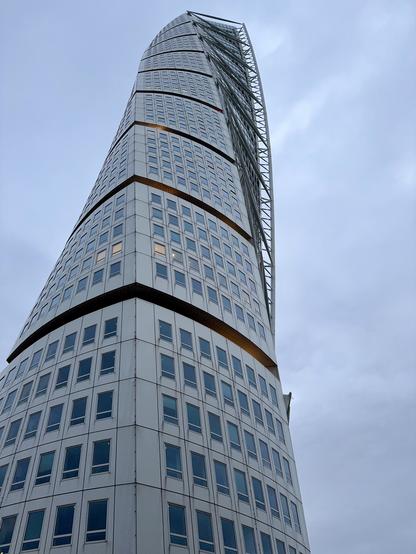A distinctive modern skyscraper with a twisting design, featuring numerous windows and a metallic exterior, set against a cloudy sky.