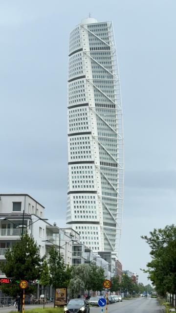A view of the Turning Torso, a modern, twisting skyscraper, surrounded by urban buildings and greenery.