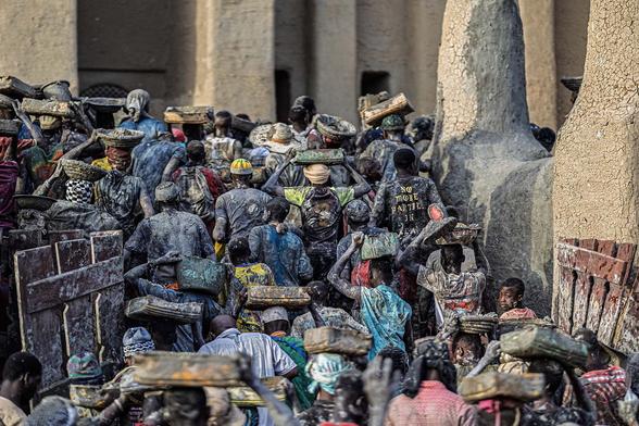 People carry buckets of mud on their heads during the re-plastering of the Great Mosque of Djenne in Djenne, on June 12, 2025. Thousands of Malians converged before dawn on the iconic mosque of Djenne, a World Heritage-listed historic town in central Mali, for the annual plastering of this earthen architectural gem. First built in the 13th century before being destroyed, the mosque was completely rebuilt in 1907 and is the largest earthen monument in the world, according to Unesco. (Photo by OUSMANE MAKAVELI / AFP)