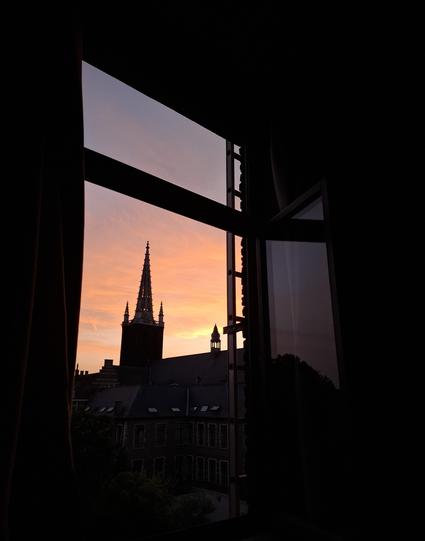 View from a dark room through a window onto the silhouette of one of the many churches during sunset in Leuven, Belgium