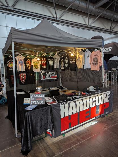 Ein Verkaufsstand der Hardcore Help Foundation mit verschiedenen Artikeln wie T-Shirts, Pullover und Mützen.