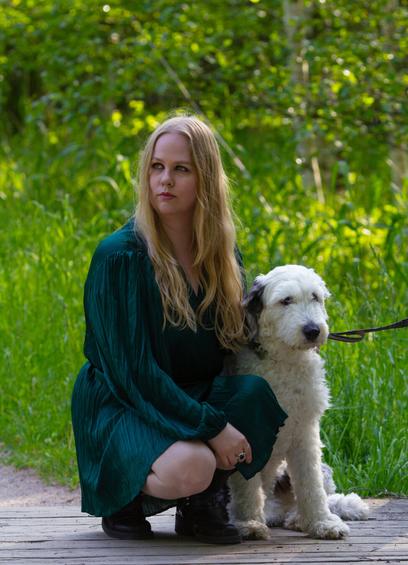 A finnish woman sitting on a peaceful nature path next to a white dog
