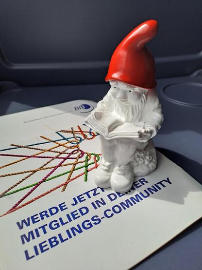 Lesender Gartenzwerg in weiß mit roter Zipfelmütze auf Flyer vom BIB mit dem Text "werde jetzt Mitglied in deiner Lieblingcommunity"