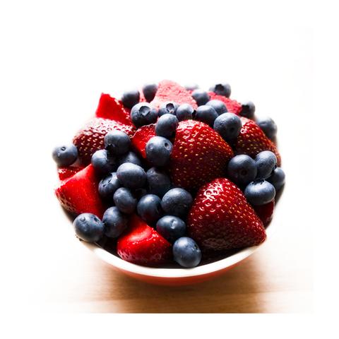 The image is presented in a square format with a clean white border. It depicts a bowl filled with fresh berries, predominantly strawberries and blueberries. The strawberries are bright red, halved or quartered, their textured surfaces catching the light. The blueberries are plump and deep blue, scattered naturally among the strawberries. The bowl itself is red with a white rim and sits on a light wooden surface. Lighting is bright and high-key, coming from above, causing soft shadows and slightly blown-out highlights at the top of the frame. This creates a clean, airy appearance. The composition is centered and emphasizes the strong color contrast between the red strawberries and blue blueberries. The fruit fills the frame almost completely.

By the end of the season, I’ll probably have washed and sliced around 50 kilos of strawberries.

And yes, I did share with my wife. ;-)