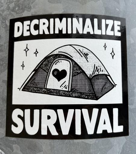 a sticker with a tent on it, reading "decriminalize survival"
