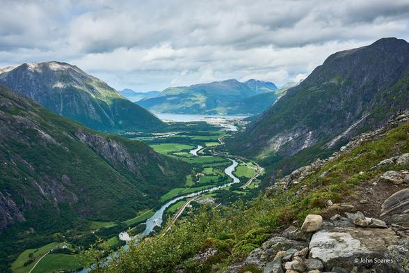 Standing on a mountain taking in the lush, fertile valley below.  The Rauma river meanders its way to Romsdalsfjorden in the background.  There are farms and buildings scattered through the green valley.  The town of Åndalsnes sits at the edge of the fjord.