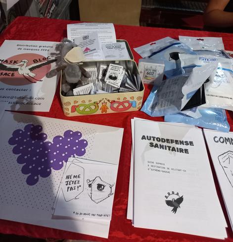 Stand du Mask Bloc avec des brochures (autodefense sanitaire, ne jette pas ton masque, pourquoi je porte un masque,...), un capteur aranet et une fourmi en peluche qui porte un masque