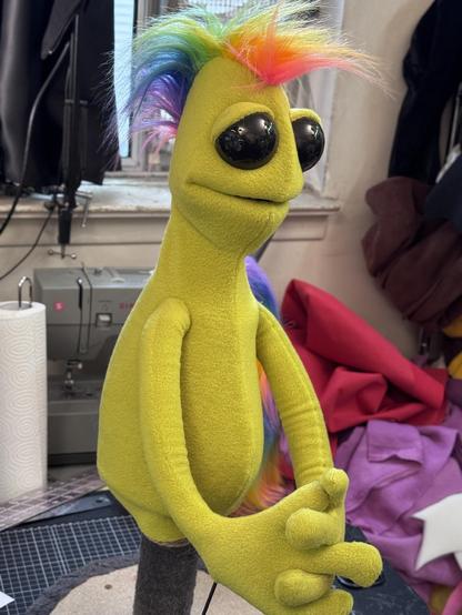 A green alien hand and rob puppet with large glossy black eyes and a rainbow Mohawk