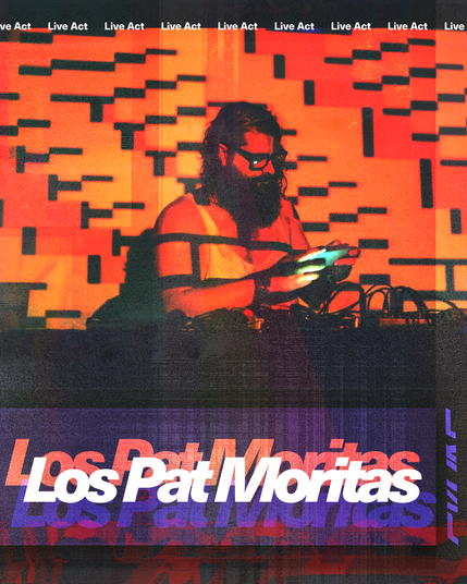 Los Pat Moritas is a man with long, dark and curly hair, big dark beard and glasses. He is playing on stage and looking at a gameboy