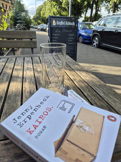 Paperback edition of the novel "Kairos" by Jenny Erpenbeck on a wooden table outside.