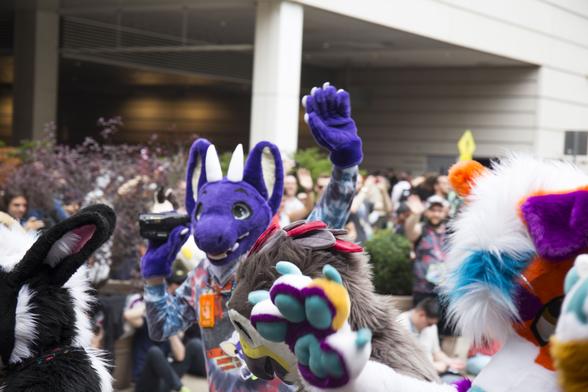 Adelair, a purple dragon fursuiter, waves in the crowd at the Anthrocon fursuit parade. Photo by Lykos.