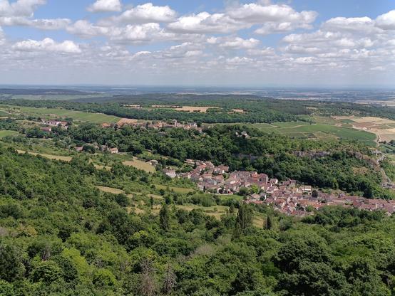 Même type de photo et de ciel, avec la suite du paysage à droite du précédent, avec une vue en perspective prise depuis le bord de la falaise. En contrebas, un village bourguignon étagé de haut à gauche en bas à droite.
Le paysage est vert et jaune, avec des forêts, des vignes et des cultures.